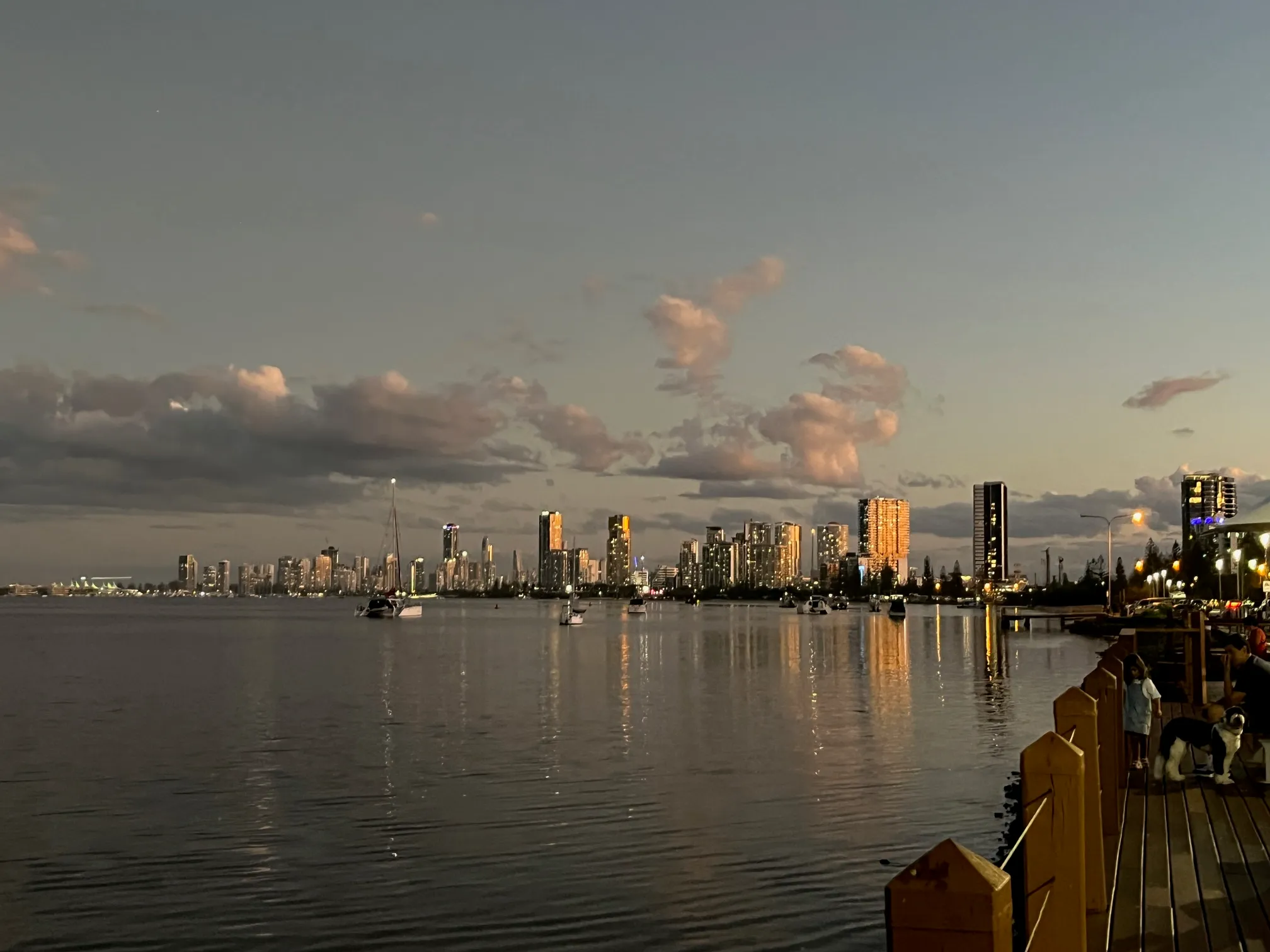 The Broadwater at dusk, looking across calm water to the lit Southport skyline, with the Labrador boardwalk railing in the foreground.
