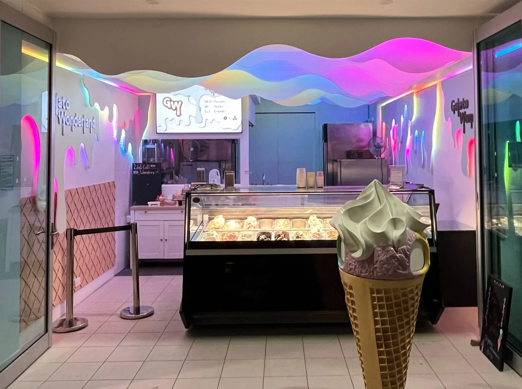 Gelato Wonderland at night in Labrador — the gelato cabinet glowing under the shop's neon wave ceiling, with a giant cone sculpture by the counter.